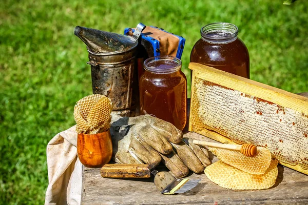 Банка свежего меда с разнообразными инструментами для пчеловодства, деревянный дозатор и поднос из пчелиного улья в натюрморте на деревянном столе на открытом воздухе с копировальным местом — стоковое фото