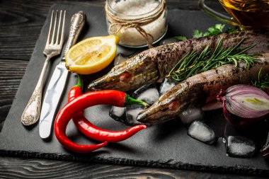 Ham nehir balığı ile limon dilimleri, otlar biberiye, tuz ve biber koyu arka plan üzerinde. Sağlıklı gıda ve beslenme kavramı. Görünümü en çok, uzay kopyalayın. Balık Pişirme için malzemeler