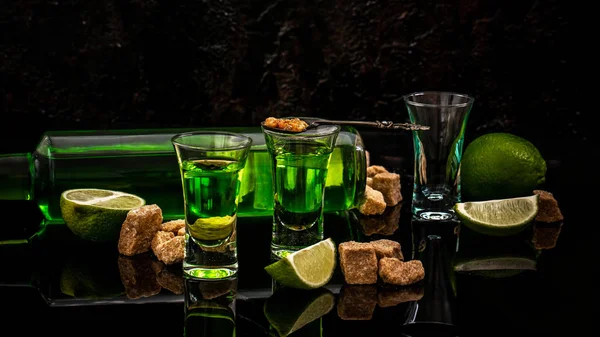 Verre de boisson alcoolisée avec sucre brun et citron vert isolé sur fond noir. Absinthe ou liqueur à la menthe avec cuillère et cubes de sucre. espace pour le texte — Photo