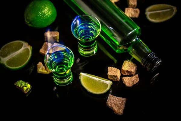 Flasche Absinth und Gläser mit brennendem Würfel braunen Zucker und Limette isoliert auf schwarzem Hintergrund. Raum für Text — Stockfoto