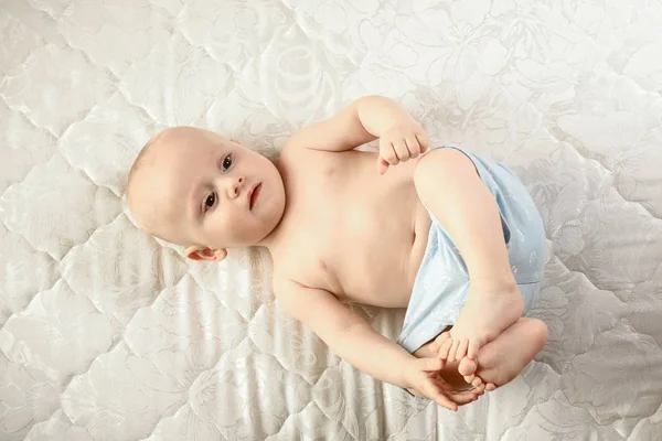 Engraçado bebê vestindo uma fralda brincando em um cobertor de malha branca. Criança após o banho ou chuveiro. Mudança de fralda infantil e cuidados com a pele. Miúdo bonito brincando com os pés — Fotografia de Stock