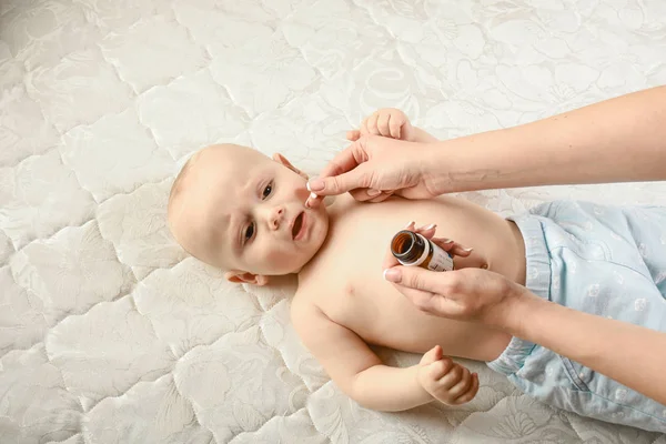 Cute sick child, baby boy, staying in bed, mom giving him medicine and checking for fever. sick infant