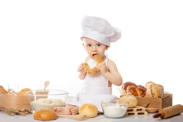 O menino com o traje do chef na frente do cesto com pão e com o bagel na mão. Cozinhar conceito de estilo de vida infantil. Criança brincando — Fotografia de Stock