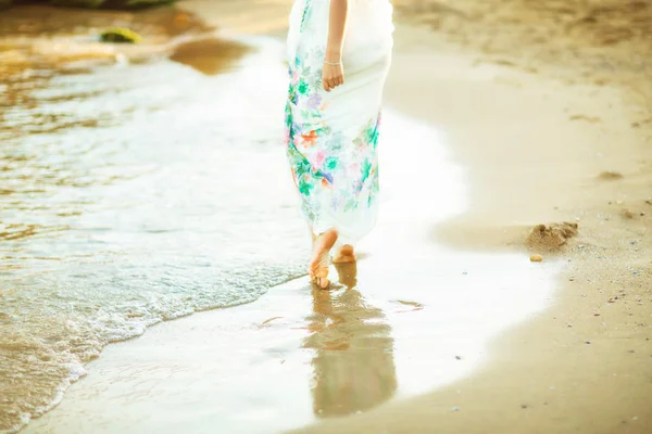 Дівчина в сукні з голими ногами на мокрому піску пляжу, вінтажний тонований фото фон — стокове фото