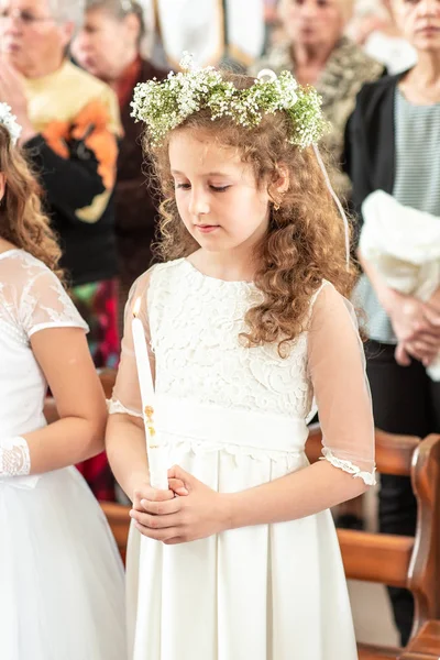 Kleines Mädchen in einem weißen, flauschigen Kleid. mit einer Kerze in der Hand. Charmantes Lächeln. Erstkommunion. — Stockfoto