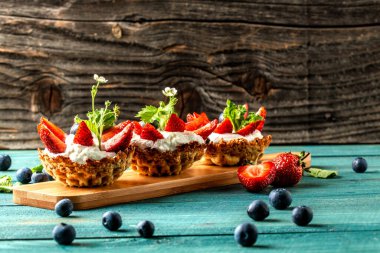 Kremalı, çilekli ve ahşap masada yaban mersinli meyveli tartlar. Metin için pankart menüsü tarifi yeri.