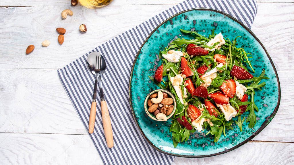 strawberry salad with arugula, brie cheese, camembert. Delicious breakfast or snack on a light background, top view.