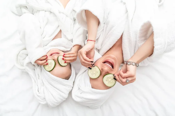 Mother and daughter had a day of spa doing face mask applying pieces of cucumber to their eyes. Beauty salon concept, wellness spa.