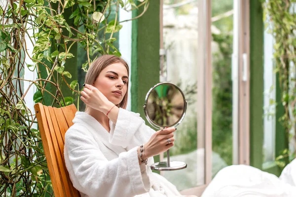 Young beautiful woman looking in the mirror. The concept of preserving the beauty of nature and youth. Spa and skin care.