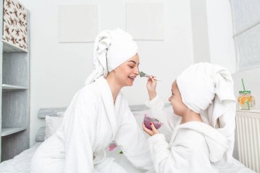 Anne ve çocuk birlikte güzellik tedavisi yapıyorlar. Mutlu aile anne ve kızı yüz maskesi yapıyor. Güzellik salonu konsepti, sağlık spası.