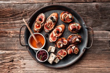 İncirli, mavi peynirli ve fındıklı metal tepsi, soğan reçeli, taze kekik, ahşap zemin üzerinde ızgara ekmek üzerine bal..