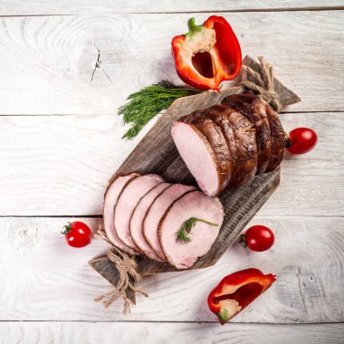 Kesme tahtasının üzerinde kurutulmuş ev yapımı jambon. Ahşap bir masada dilimlenmiş tütsülenmiş tavla, organik tarım ürünleri..