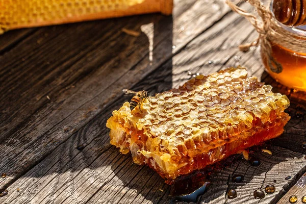 蜂の飛行 蜂蜜の完全な細胞と蜂蜜木製のテーブルの上に木製の蜂蜜紙 蜂の飛行とガラス瓶の中の蜂蜜 — ストック写真