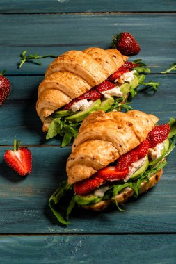 Kahvaltı, iş yemeği, çilekli kruvasan sandviçi ve ahşap arka planda küflü krem peynirli peynir. Pankart menü tarifi üst görünümü.