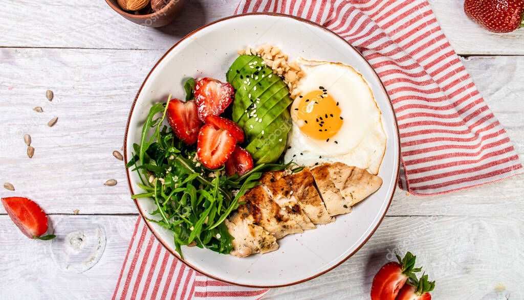 Trendy salad. Vegan Buddha bowl with Chicken salad with arugula and strawberries. Delicious breakfast or snack on a light background, top view.