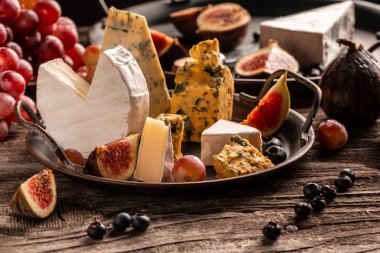 Lezzetli gurme peyniri, dilimlenmiş taze incir ve üzümlerle servis edilen yumuşak peynirlerin kırsal ahşap arka planda servis edilmesi, yemek servisi, afiş, menü, tarif, metin için yer.