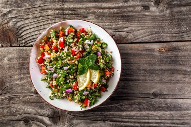 Kuskus, sebze ve otları koyu ahşap bir arka planda kahverengi bir kasede olan doğu tabbouleh salatası. Boşluğu kopyala