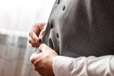 Damat sabah toplantılarında yeleğinin düğmesini bağlar. Damat düğmeyi bağlar. Düğün günü. Gri ceket. Damadın elleri, damatların sabah hazırlığı.
