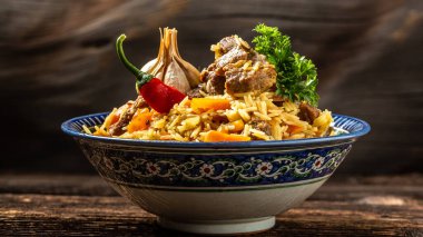 Geleneksel Özbek yemeği Pilaf tabağında koyu ahşap bir arka planda doğu süsüsüyle. Orta Asya mutfağı, uzun pankart biçimi.