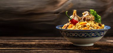 Pilav denilen geleneksel Özbek yemeği. Tabakta et ve siyah ahşap arka planda doğu süsü olan pirinç, uzun afiş formatı. Metin için boşluk.