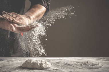 Un ve un serpintili erkek eli fotoğrafı. Ekmek pişiriyorum. Hamuru yoğurmak. Karanlık arka planda izole edilmiş. Metin için boş boşluk.
