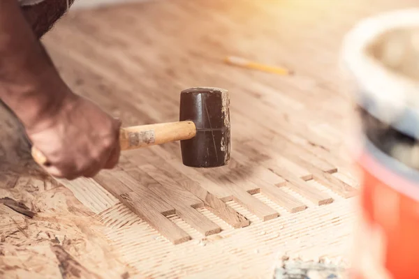 close up hands of Carpenter on work laying laminate or parquet flooring use a rubber mallet, Worker installing wooden laminate flooring.