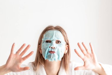 Yüzünde maskeyle poz veren güzel beyaz bir bayan evde güzellik prosedürlerinin tadını çıkarıyor. Spa prosedürleri.