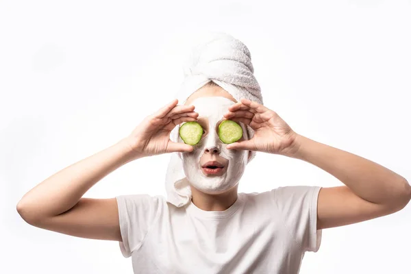 happy child girl in towel with mask on face and cucumber on eyes getting beauty tretment. concept of natural cosmetics for young skin.