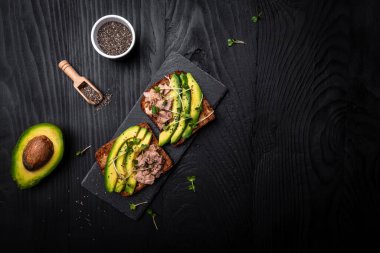 Avokado ve ton balıklı sandviç, mikroyeşil. Ton balıklı tostlar koyu arka planda sağlıklı yemekler, üst manzara, düz yatış..