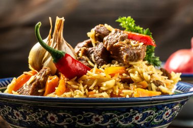 Pilav denilen geleneksel Özbek yemeği. Tabakta et ve siyah ahşap arka planda doğu süsü olan pirinç, uzun afiş formatı. Metin için boşluk.