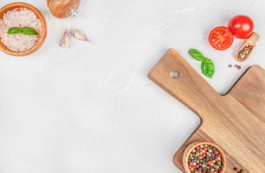 Domatesli, sarımsaklı, fesleğenli, karabiberli ve beyaz arka planda tuz içeren tahta kesme manzarası. Boşluğu kopyala.