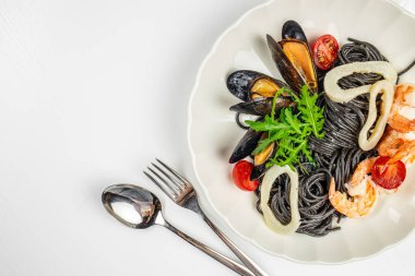 Beyaz tabakta deniz ürünleri, midye, karides, kalamar ve vişneli domatesli siyah mürekkep balığı makarnası. Boşluğu kopyala, üst görünüm.