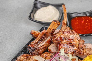 Izgara kuzu pirzola soslu ve soğanlı siyah tabakta fotokopi alanı ile.