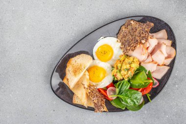 Yağda yumurta, hindi dilimleri, salata, avokado ve siyah tabakta kızarmış ekmek ile sağlıklı kahvaltı. Reklam ve menü için fotokopi alanı olan üst manzara..