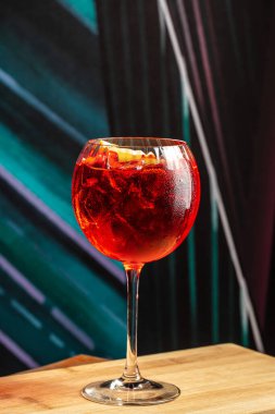 Kırmızı kokteyli buz ve portakal dilimli ahşap masadaki şarap kadehiyle tazeliyorum..