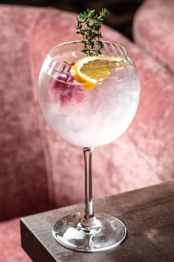 Limon dilimli soğuk cin tonik kokteyli ve ahşap masadaki şarap kadehinde bitkiler..