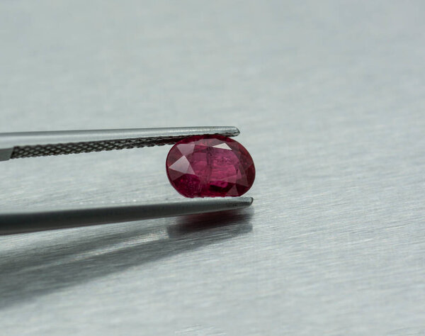 Precious ruby stone carved and fastened with tweezers on metal background