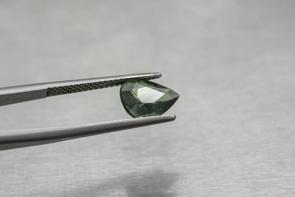 Carved green sapphire held with tweezers on metal background