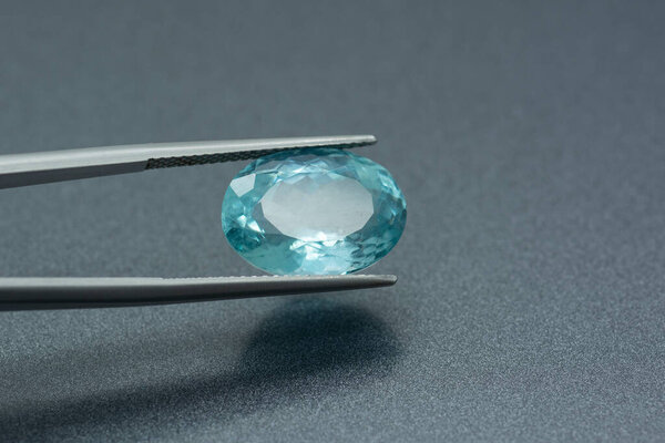Макроизображение резного аквамарина, зажатого на сером металлическом фоне