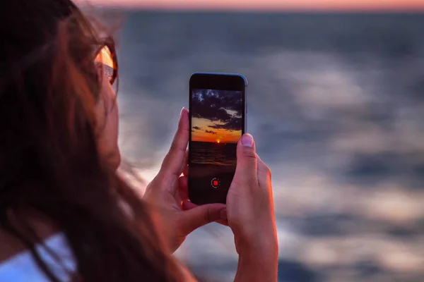 Tangan wanita memegang ponsel pintar untuk mengambil selang waktu matahari terbenam di pantai. telepon seluler dengan tampilan di layar saat matahari terbenam — Stok Foto