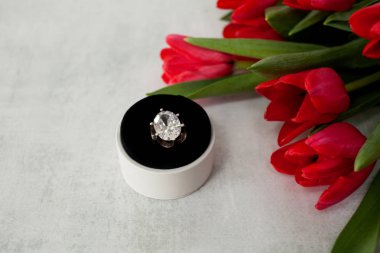 Üstten Görünüm nişan yüzüğü keskinleştirme gri arka plan üzerinde yuvarlak beyaz kutu içinde dev elmas ve bir buket kırmızı lale