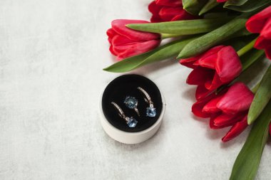 Üst görünüm yüzük ve küpeler ile Topaz ve elmas bir yuvarlak beyaz kutu üzerinde bir keskinleştirme gri arka plan ve kırmızı lale bir buket