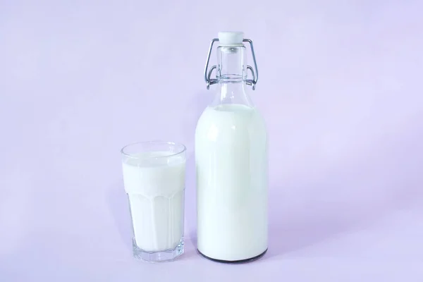 Latte fresco a colazione in bottiglia di vetro e un bicchiere di latte al centro della cornice su fondo lavanda — Foto Stock