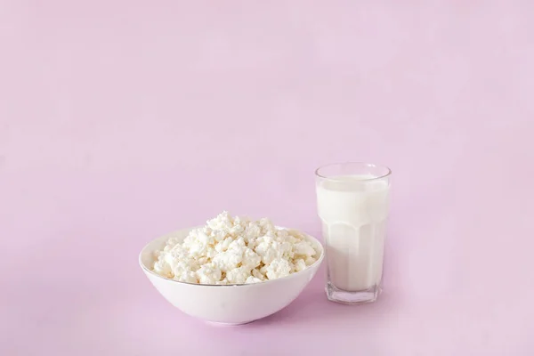 Frischer Quark zum Frühstück in einer weißen Schüssel und ein Glas Milch in der Mitte des Rahmens auf rosa Hintergrund — Stockfoto