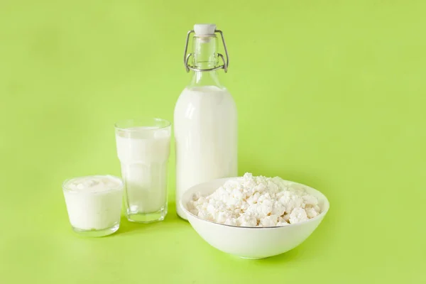 Latte in una bottiglia fiocchi di latte alla panna acida e un bicchiere di latte su uno sfondo verde — Foto Stock
