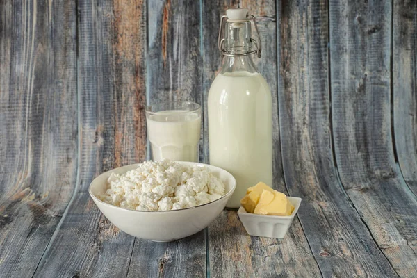 Latte in una bottiglia burro ricotta e un bicchiere di latte su uno sfondo di legno — Foto Stock