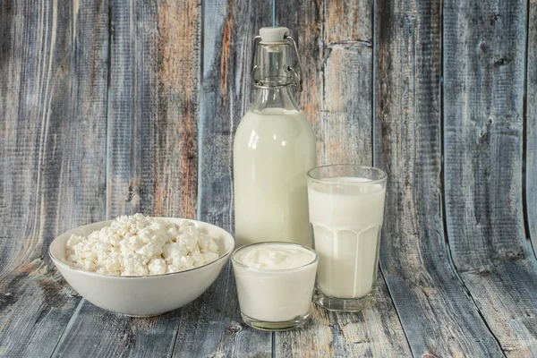 Latte in una bottiglia fiocchi di latte alla panna acida e un bicchiere di latte su uno sfondo di legno — Foto Stock