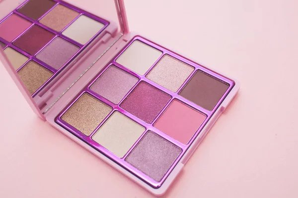 close up view Palette of multicolor cosmetic make up with a mirror on pink background, pink eye shadow palette