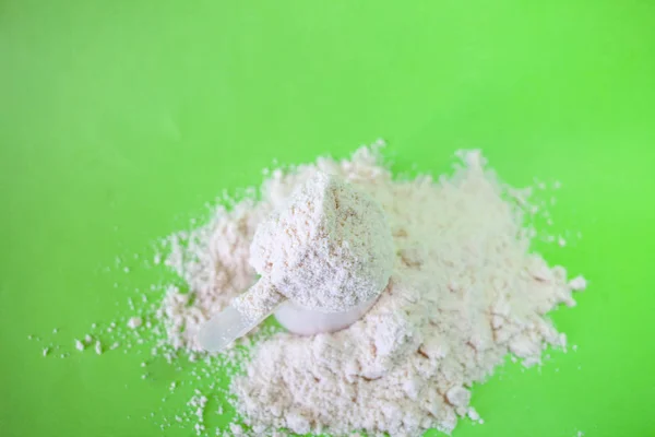 Heap of whey protein powder with plastic spoon on green background — Stock Photo, Image