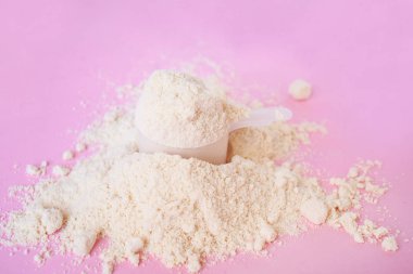 açık pembe arka plan üzerinde plastik kaşık ile peynir altı suyu protein tozu yığını
